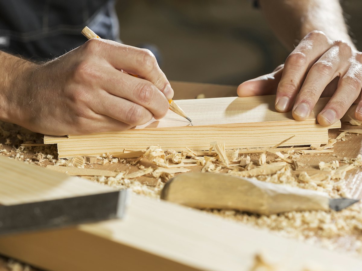 Hände markieren mit Bleistift ein Maß auf einem Holzbrett